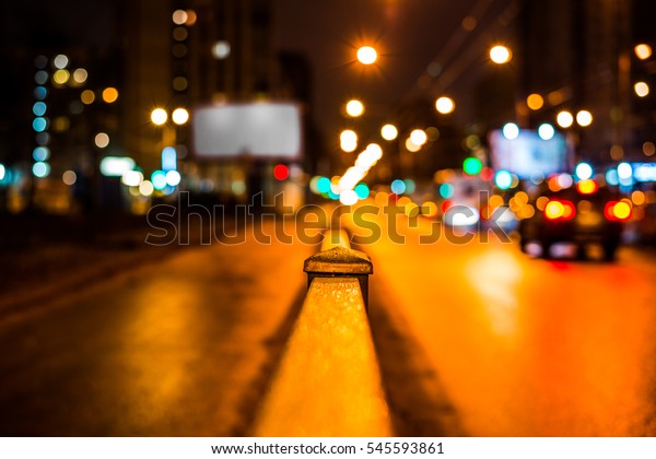 Dark night in the big city, pavement with billboard\
and the road on which the car ride. Close up view from the handrail\
on the sidewalk level