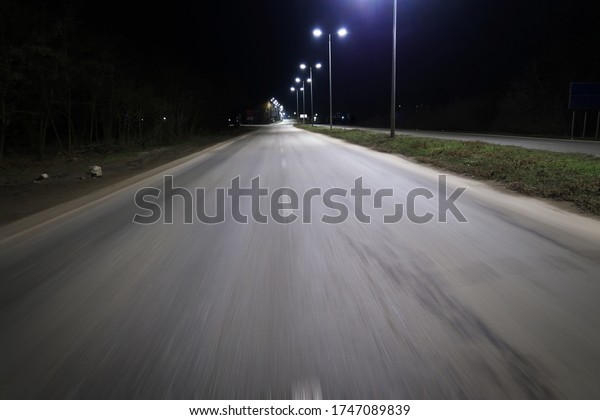 Dark\
night empty asphalt road in motion and\
lampposts