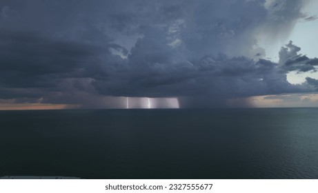 Dark ominous thunderstorm clouds forming on overcast sky during heavy rainfall season over ocean surface at sunset - Powered by Shutterstock