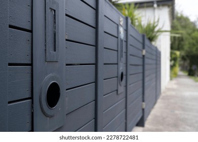 Dark painted wooden garden gate with a letterbox with vertical slot and below it a tube in which newspapers can be deposited. Focus on the left - Shutterstock ID 2278722481