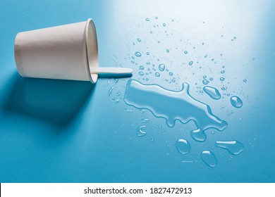 Dark Paper Cup With Abstract Drops Of Spilled Water On Blue Background. Spilled Alcohol Drink Cup Concept.