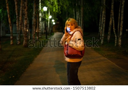In a dark Park on the path is a woman, she is afraid, street lights Shine, it is dark around.