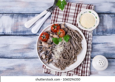 Dark pasta with vegetables in white sauce on wooden background. Selective focus.