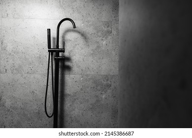 Dark photo of black floor-standing bath tap, on background of grey wall.