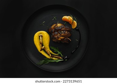 Dark photo of a fine dining dish with duck breast and roasted squash purée, mushrooms and greens. Black background with studio professional lighting in a top view, flat lay. Stylish gourmet plating.