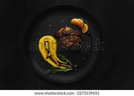 Dark photo of a fine dining dish with duck breast and roasted squash purée, mushrooms and greens. Black background with studio professional lighting in a top view, flat lay. Stylish gourmet plating.