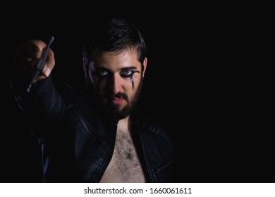 Dark Portrait Of Modern Shaman Young Man With Viking Painting. Handsome Serious Bearded Guy With Painted Face And Bloody Sword On His Hands On Black Background. Concept Of People Emotions