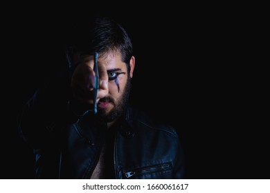 Dark Portrait Of Modern Shaman Young Man With Viking Painting. Handsome Serious Bearded Guy With Painted Face And Bloody Sword On His Hands On Black Background. Concept Of People Emotions