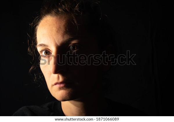 Dark\
portrait of a serious woman with her face partially lit. The woman\
is staring blankly showing sadness or\
anxiety