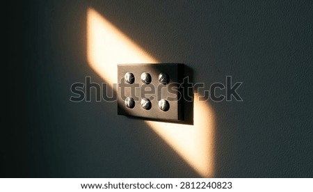 A dark, rectangular object with six evenly spaced circular indentations is dramatically lit by a diagonal beam of warm sunlight against a dark background.