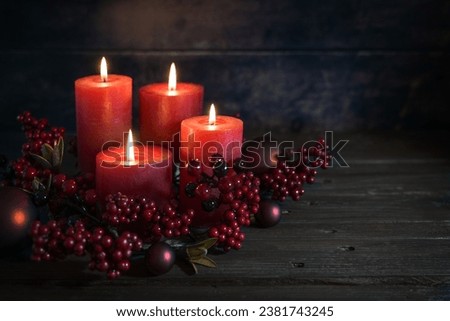 Dark red advent decoration with for lit candles, berrie decoration and Christmas balls against a rustic wooden background, copy space, selected focus, narrow depth of field