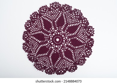 A dark red crochet doily on a white background