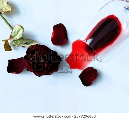 Dark romantic flat lay featuring a spilled wine glass, dried rose, and scattered petals on a white background. Aesthetic composition evoking themes of heartbreak, passion, and lost love.