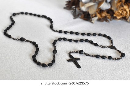 Dark rosary for prayers on a light background, dried flower in natural colors