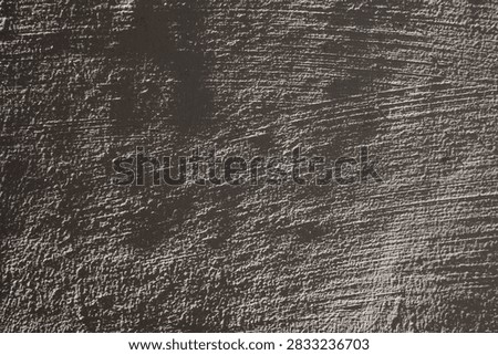 Dark rough plaster surface with brush marks, ridges and deep shadows, enhanced by harsh side lighting for industrial, architectural, grunge, abstract, and textured background designs