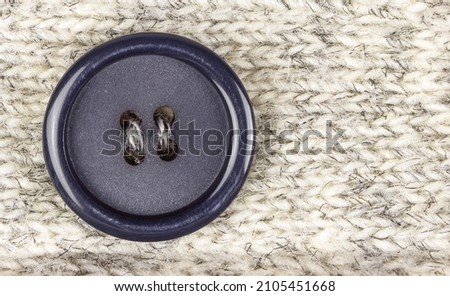 Dark round sewn button in knitted man-made fiber fabrics