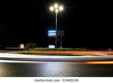 A dark roundabout at night near the TT circuit in Assen, the Netherlands. Passing cars create beautiful light trails.