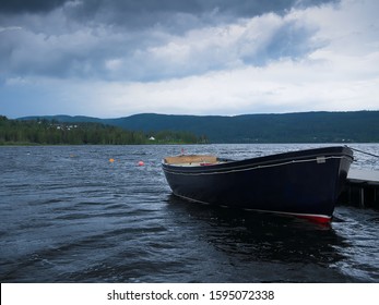 Dark Row Boat Tied To A Dock On Beautiful Lake Hurdalssjoen In Norway, With Storm Clouds Overhead. Beautiful Europe Travel Scene.