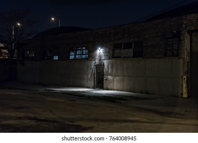 Dark Scary Alley At Night With Gated Door Warehouse Entrance.
