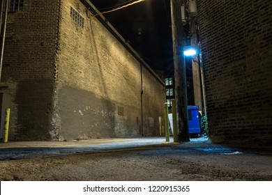 Dark And Scary Downtown Urban City Street Corner Alley With An Eerie Vintage Industrial Warehouse Factory And A Dirty Dumpster At Night
