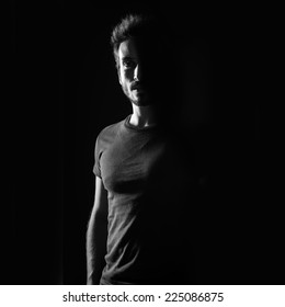 Dark Shadow Portrait Of Confident Young Man Wearing Shirt Against Black Background. Black And White Image. 