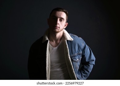 Dark shadow portrait of confident young man wearing jeans jacet against black background. Looking at camera