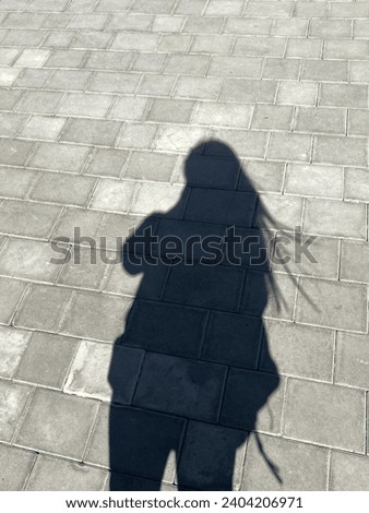 A dark shadow of a woman with wavy hair on the ground on a sunny day