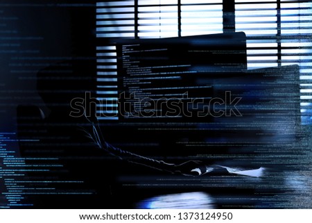 Dark silhouette of cyber criminal hacking computer behind digital symbols