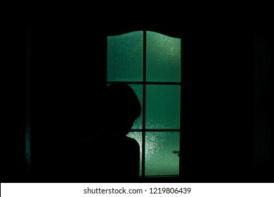 Dark silhouette of kid behind glass in supernatural green light. Locked alone in room behind door on Halloween. Nightmare of child with aliens, monsters and ghosts. Evil in home. Inside haunted house.