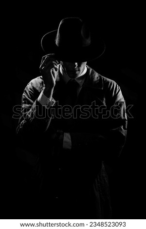 A dark silhouette of a man in a coat and hat in the noir style. A dramatic portrait in the style of detective films of the 1950s and 60s. The silhouette of a spy. monochrome