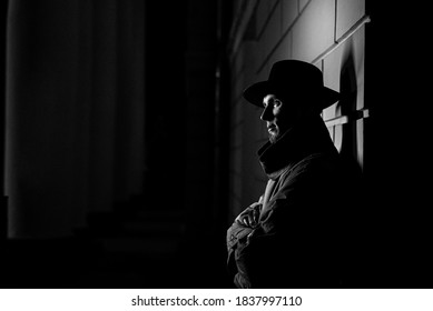 dark silhouette of a man in a raincoat with a hat and a scar on his face at night in a crime Noir style