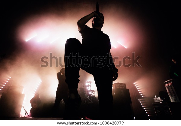 A\
dark silhouette of a singer on the stage. Good-looking background,\
bright stag lights. A concert of a famous music\
band