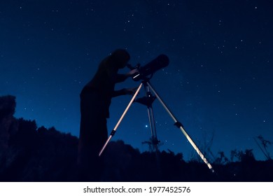 Dark silhouette of a sky watcher of the starry sky in a telescope. Woman observer watching the night sky in a reflector.