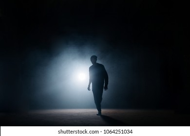 dark silhouette of slim man walking on the street at night. being alone. lighted street. thief sneaking in the street.night crime - Shutterstock ID 1064251034