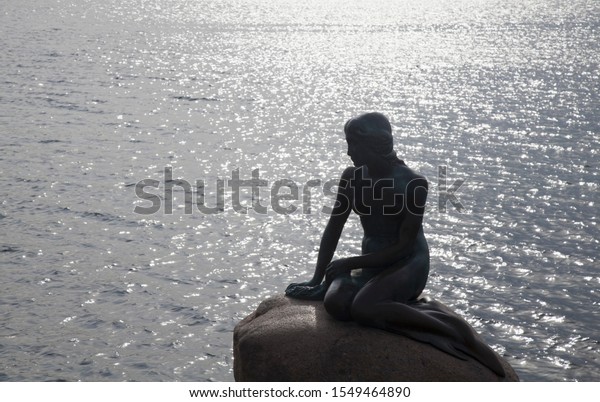 Dark silhouette of statue of little mermaid on stone\
against water waves 