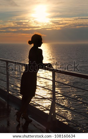dark silhouette of woman looking into distance and standing on deck at sunset
