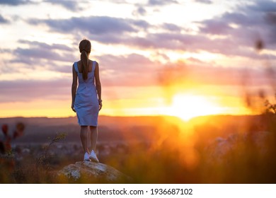 Dunkle Silhouette einer jungen Frau in Sommerkleid stehen draußen und genießen Blick auf die Natur bei Sonnenuntergang.