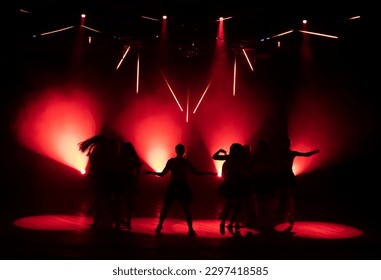Dark silhouettes of dancing girls against the background of red light from stage spotlights. - Shutterstock ID 2297418585