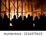 Dark silhouettes of people against the backdrop of a giant raging fire at night. The dark figures of a people against the backdrop of a burning wooden building at night. People and a giant fire blast.