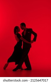 Dark silhouettes of tango dancers couple on red background. Man in classic suit and woman in elegant dress in dancing movement.