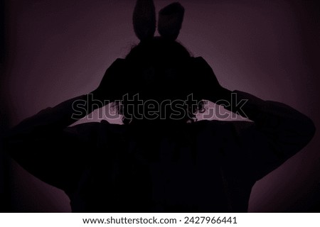 Dark silhuette of girl in easter bunny ears against pink background