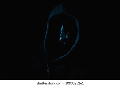 Dark and sinister with a mask on figure in a hood against a black background - Powered by Shutterstock