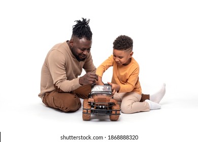 Dark skinned African male and his little son spend time together.  They sit on the floor and have fun with a toy car against white background in studio - Powered by Shutterstock