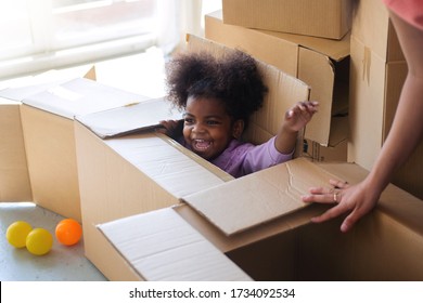 Dark Skinned Child Girl Playing In Cardboard Box In Room, Hiding In A Box While Playing Hide And Seek 