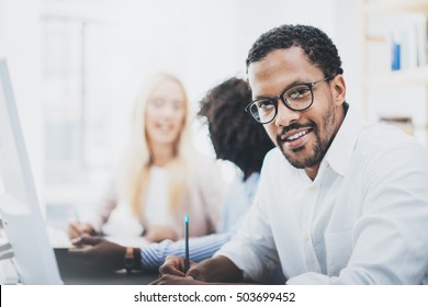 Dark Skinned Entrepreneur Wearing Glasses, Working In Modern Office.African American Man In White Shirt Looking And Smiling At The Camera.Horizontal,blurred Background.