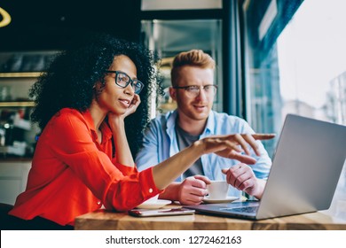 Dark skinned female graphic designer pointing with finger on laptop computer during collaboration with caucasian colleague on common project in coffee shop.Two multicultural friends discussing website - Shutterstock ID 1272462163