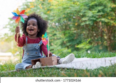 Dark skinned little girl blowing windmill, cute little girl holding colorful toy pinwheels on summer day