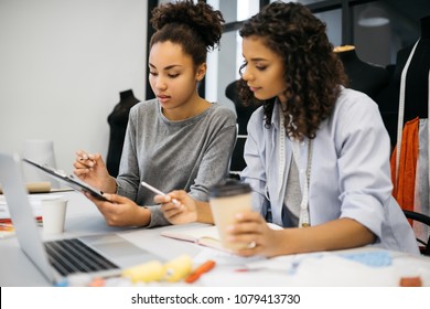 Dark skinned stylish women working together in creative office, drawing, sketching, drinking coffee. Concentrated hipsters learning fashion and design at loft modern atelier. Brainstorming. Startup.  - Powered by Shutterstock