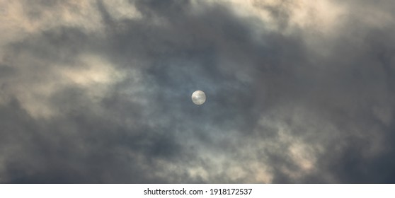 The dark sky is covered with continuous clouds, through which the dim sun barely sees
