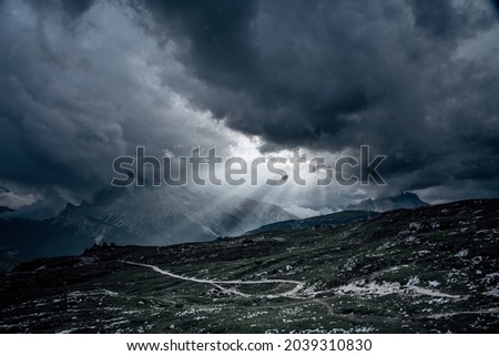 Dark sky in the mountains before sunset. Sun rays, dark clouds on the sky, dark green grass and many stones on the hills.